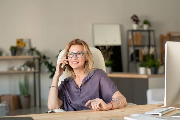 Businesswoman talking over smart phone in home office seen through window